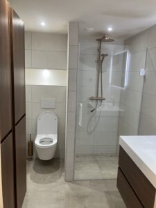 Strakke badkamer met koperen regendouche, inbouwtoilet en houten kasten