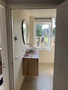 Badkamer met houten wastafelmeubel, ronde spiegel en waskom