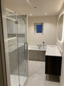 Badkamer met glazen douchewand, ligbad en houten wastafelmeubel